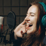 mujer joven cantando con cascos y expresión de felicidad frente a micrófono de estudio