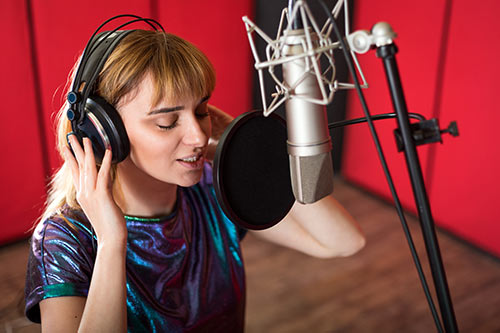 mujer joven cantando con manos en los cascos frente a micrófono de estudio