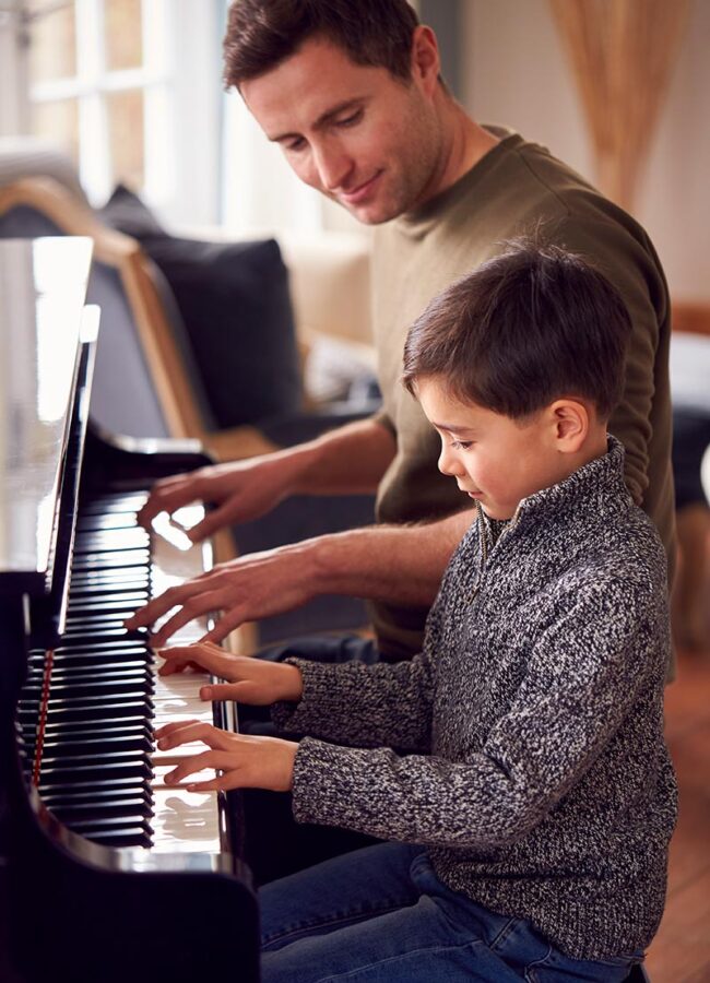 Niño muy pequeño tocando el piano junto a su profesor en clase de música.