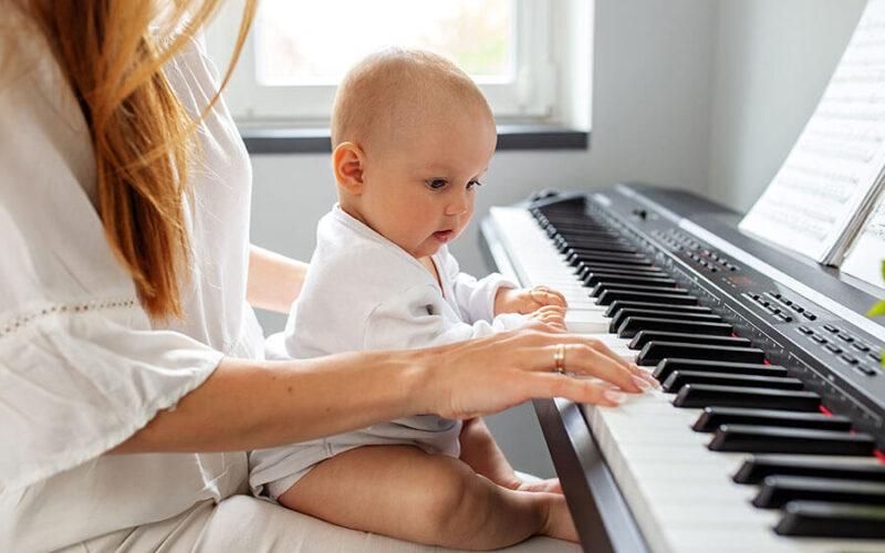 Bebé en el regazo de su madre, tocando las teclas de un piano en clases de estimulación musical.