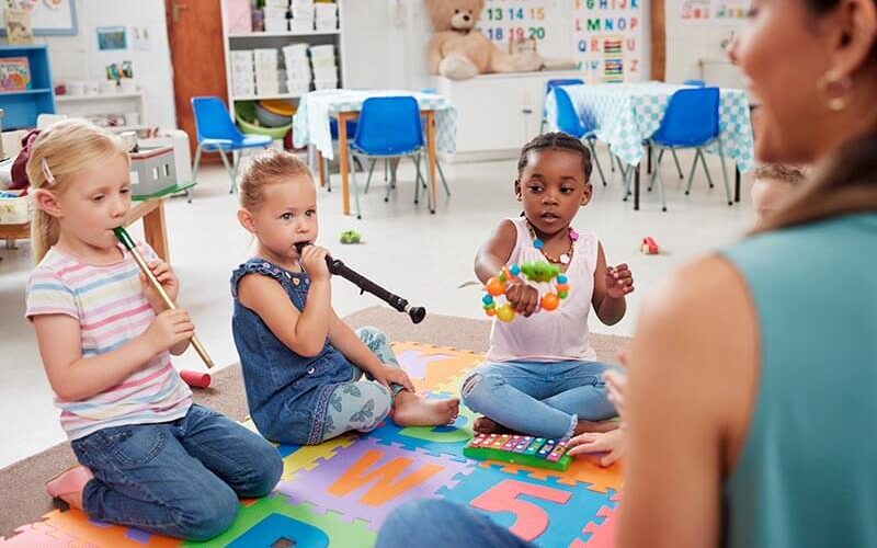 Niñas pequeñas tocando integumentos musicales junto a profesora de sensibilización musical.